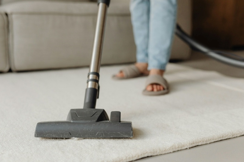 Vacuuming beige low-pile rug on wooden flooring